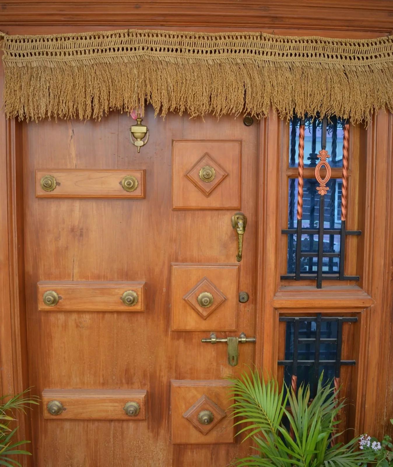 A paddy toran hung across the top of a carved wooden front door