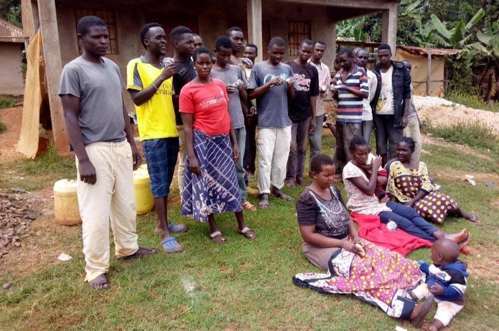 Young carvers and women of the community holding small soapstone pieces outside a house in Kisii
