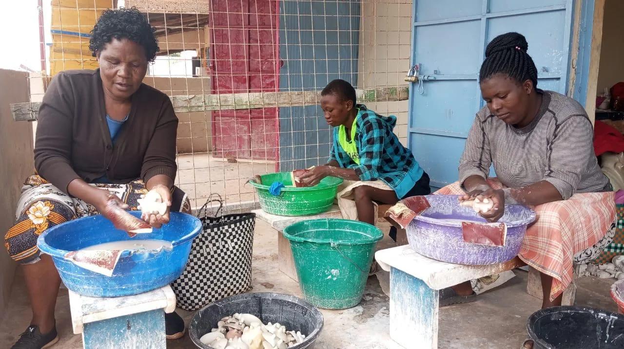 Three women sanding and polishing soapstone pieces in basins of water