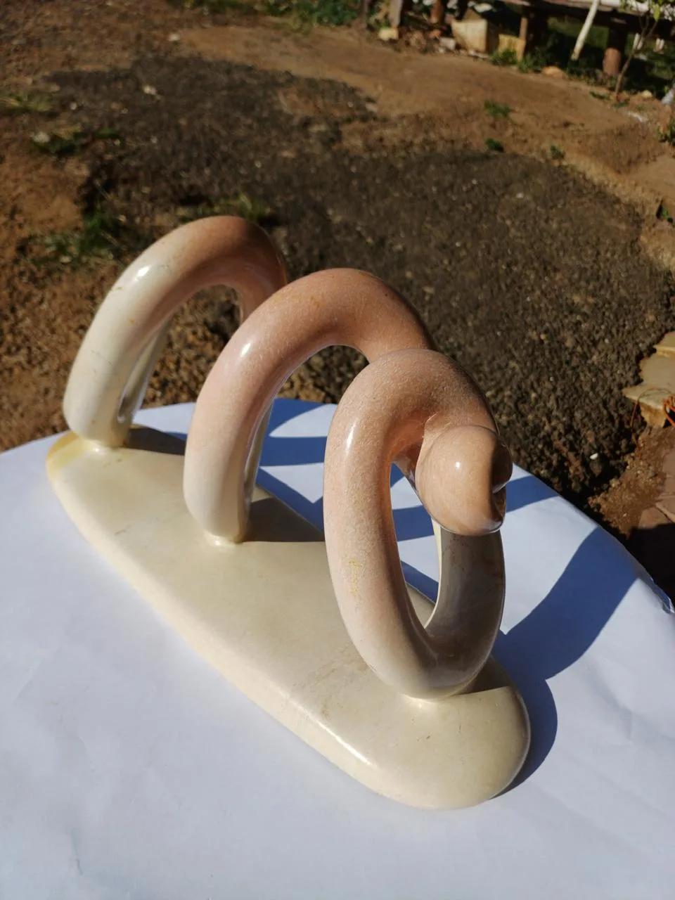 A polished abstract soapstone sculpture of three cream-and-pink loops on a base